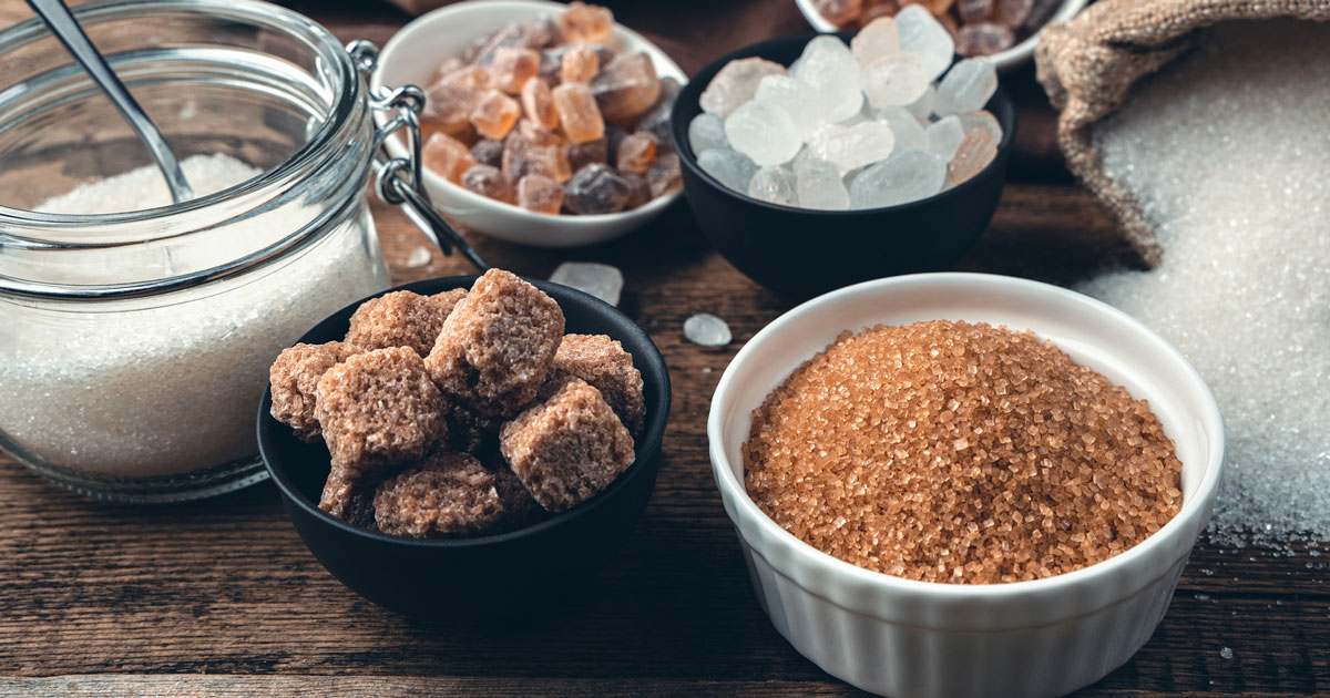 Assorted types of sugar including brown sugar, white sugar, and brown sugar cubes on a wooden surface.
