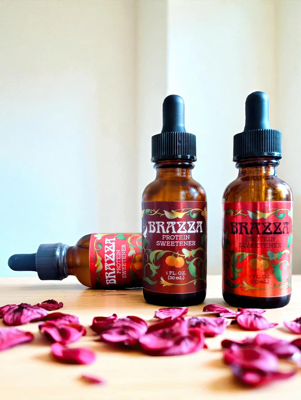 Three bottles of Brazza sweetener on a wooden board with petals strewn