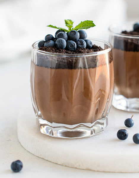 Chocolate dessert in a glass with blueberries and mint leaves on a white background