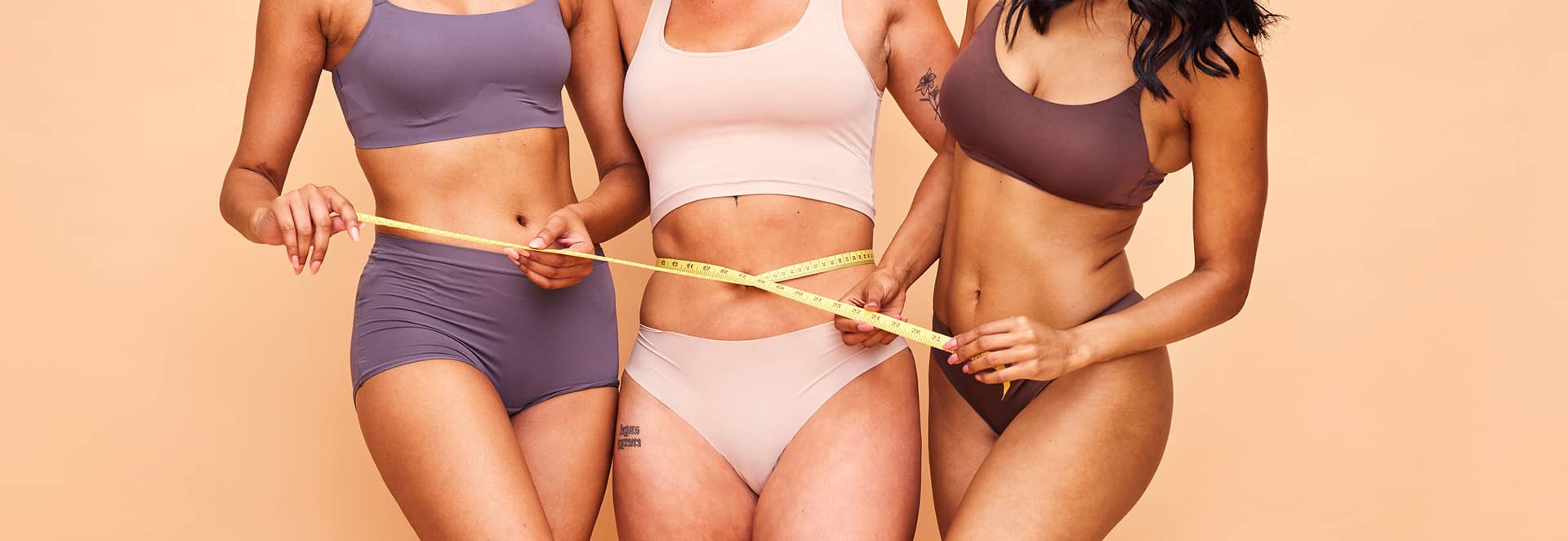 Three women measuring their waists with a tape measure against a beige background