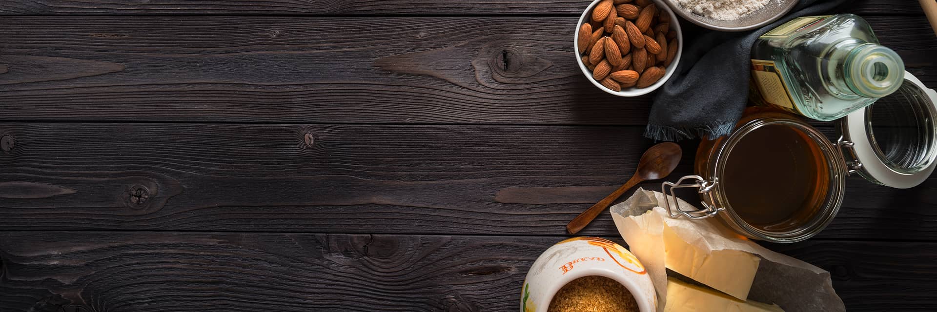 Assorted food items including a jar of jam, a bowl of nuts, and a bottle of oil on a wooden surface.