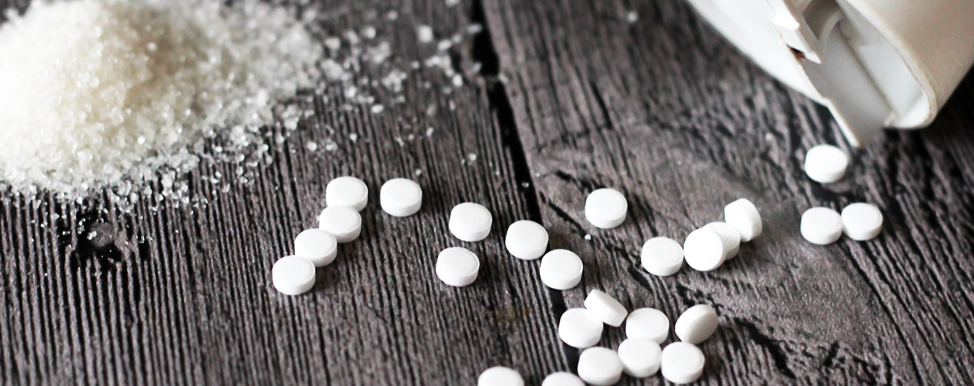 Chemical sweetener pills on a wooden surface with a light source above